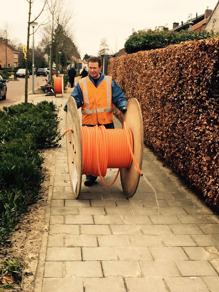 Man rolling spool of fiber down sidewalk